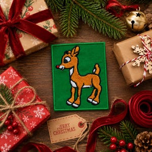 May include: A rectangular embroidered patch featuring a cartoon reindeer with brown fur, a white belly, and a bright red nose on a solid green background. The patch is surrounded by various holiday-themed gift boxes and festive decorations.