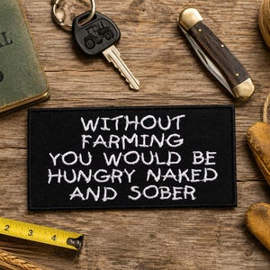 May include: A rectangular black embroidered patch with white text that reads WITHOUT FARMING YOU WOULD BE HUNGRY NAKED AND SOBER. The patch is surrounded by a green book, a tractor key, a pocket knife, a tape measure, twine, and leather gloves.