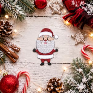 May include: An embroidered patch of Santa Claus featuring a red hat with a white pom-pom, a thick white beard, a red coat with white trim, and black boots. The figure has a peach-colored face with a small red nose and a simple mouth expression.