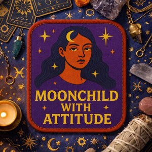 May include: A rectangular fabric patch with a dark purple background featuring an illustration of a person with long dark hair and a crescent moon on their forehead. The text reads MOONCHILD WITH ATTITUDE in yellow letters, surrounded by yellow stars.