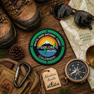May include: An outdoor adventure scene featuring hiking boots, sunglasses, a compass, and a map. A circular patch with the text "White River National Forest" and "Explore More Colorado" is also present, along with a tag that says "Adventure Awaits."