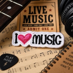 May include: An assortment of music-themed items on sheet music. Includes a guitar fretboard, a patch that says "I ❤️ MUSIC", a black guitar pick, headphones, and a notebook with text.
