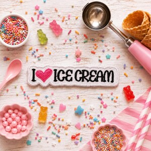 May include: A white embroidered patch with black text reading I LOVE ICE CREAM and a pink heart, surrounded by colorful sprinkles, gummy bears, a pink ice cream scoop, two waffle cones, a pink spoon, and two small bowls filled with sprinkles.