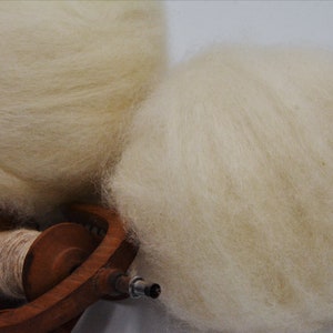 May include: Two balls of white wool fibre, one on top of a wooden spinning wheel.