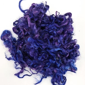 May include: A pile of blue and purple curly fiber, likely wool or alpaca, for spinning or felting.