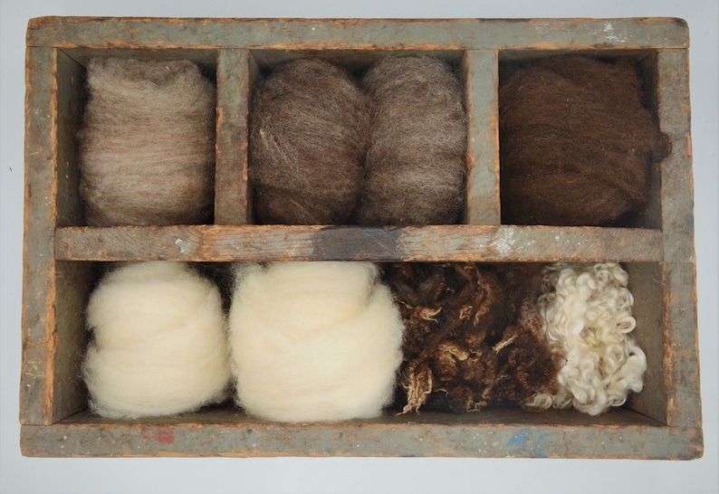 May include: A wooden divided box filled with various shades of wool. The wool ranges in color from light beige to dark brown. The box has a weathered, rustic appearance, suggesting it is vintage or handmade.