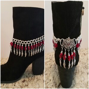 May include: A pair of black ankle boots with a silver chain and red crystal accents. The chain has small silver feather charms hanging from it.
