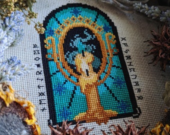 May include: Cross-stitch embroidery of a blue and gold ornate mirror with a crown and runes around the border. The mirror is surrounded by a black frame.