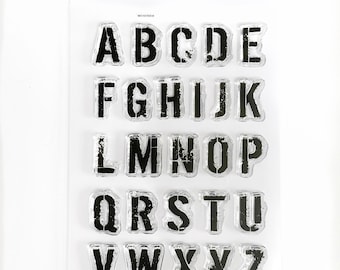 May include: Clear stamp set with the alphabet in a distressed font. The letters are black and the background is clear. The stamp set is packaged in a clear plastic sheet with the brand name "Craftily by Toni" printed on the top.