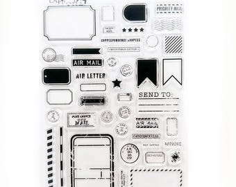 May include: Clear acrylic stamp set featuring various postal-themed designs. Includes stamps with text like "Air Mail," "Priority Mail," and "Confidential." Also includes frames, stars, and other decorative elements for crafting.