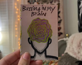 Puede incluir: Una pequeña obra de arte rectangular con las palabras "Buzzing in My Brain" en letras verdes. La obra presenta un contorno negro de una cabeza con un diseño arremolinado de varias capas en forma de cerebro, coloreado en tonos morados y verdes.