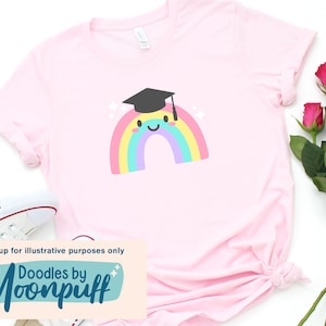 Puede incluir: Una camiseta rosa con un gr&aacute;fico de arco&iacute;ris que lleva una gorra de graduaci&oacute;n. El arco&iacute;ris tiene una cara sonriente. El texto "Doodles by Moonpuff" est&aacute; en la parte inferior de la camiseta.