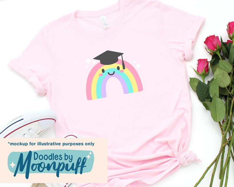 Puede incluir: Una camiseta rosa con un gr&aacute;fico de arco&iacute;ris que lleva una gorra de graduaci&oacute;n. El arco&iacute;ris tiene una cara sonriente. El texto "Doodles by Moonpuff" est&aacute; en la parte inferior de la camiseta.