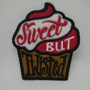 Peut inclure: Écusson brodé en forme de cupcake avec les mots "Sweet BUT Twisted". Le cupcake a un glaçage rouge et blanc, une base marron et des contours noirs. Le texte est en écriture cursive.