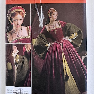 May include: Simplicity sewing pattern 2589 for a historical-style gown. The envelope features a burgundy velvet dress with wide, patterned sleeves, a gold underskirt, and a matching headpiece. Text includes pattern number 2589, sizes U5 16, 18, 20, 22, 24, and EUR 42-50.
