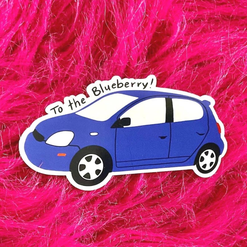 May include: A blue car sticker with the text "To the Blueberry!" in white. The sticker features a cartoon-style car with black wheels and white windows, set against a vibrant pink background.