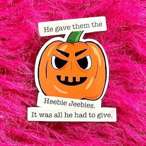 May include: A Halloween-themed sticker featuring an orange jack-o'-lantern with a stern expression. The sticker includes the text "He gave them the Heebie Jeebies. It was all he had to give." The background is a vibrant pink, fluffy texture.
