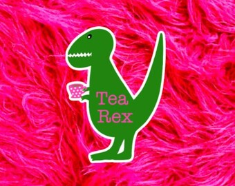 May include: A green dinosaur sticker featuring a small pink polka-dot teacup held in its hand. The text Tea Rex is printed in pink on the body of the dinosaur. The sticker has a white border and is displayed against a bright hot pink fuzzy background.