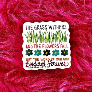 May include: White sticker with green grass and blue flowers. The text reads "The grass withers and the flowers fall but the word of our God endures forever. Isaiah 40:8"