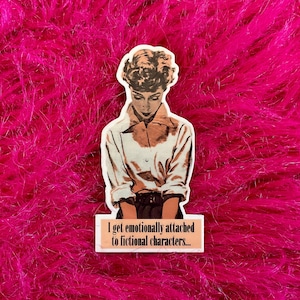 May include: A sticker with a vintage illustration of a woman with short hair, wearing a white shirt and dark pants. The sticker has the text "I get emotionally attached to fictional characters..." printed on it.