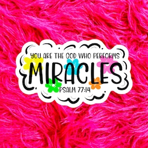 May include: A white sticker with the text "YOU ARE THE GOD WHO PERFORMS MIRACLES" in black, with colorful flower accents. The sticker also includes "PSALM 77:14". The background is a vibrant pink, fluffy texture.