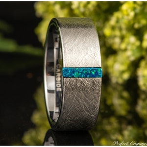 May include: A silver tungsten carbide ring with a brushed finish and a blue opal inlay. The ring has the word "CARBIDE" engraved on the side.