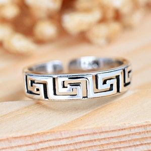 May include: Silver ring with a geometric design. The ring is adjustable and has a Greek key pattern.