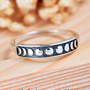 May include: A silver ring with a band of eight moon phases, each phase is a raised circle with a black crescent moon design.
