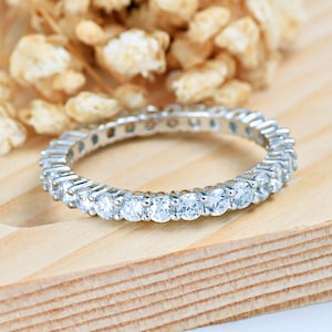 May include: A silver eternity band with a row of small, round, clear gemstones.