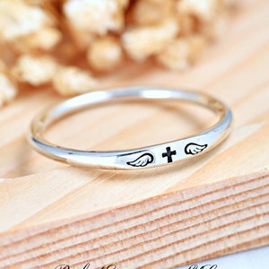 May include: A silver ring with a cross and angel wings engraved on the band.
