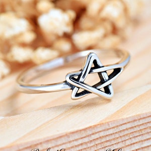May include: A silver ring with a five-pointed star design. The star is made of intertwined lines, creating a delicate and intricate pattern.