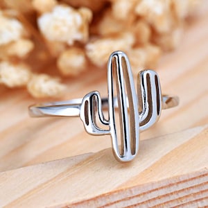 May include: A silver ring with a cactus design. The cactus is outlined and has a textured look.