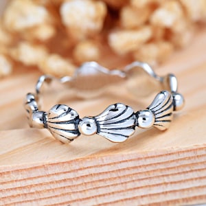 May include: Silver ring with a design of three seashells. The ring is on a wooden surface.