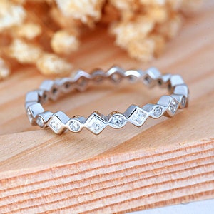 May include: A silver band ring with a row of small, clear, square-shaped stones set in a scalloped design.