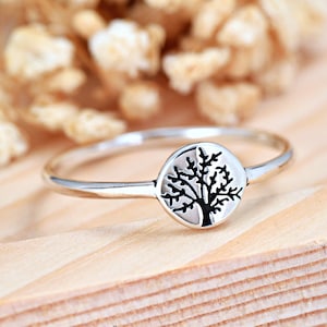 May include: A silver ring with a round tree design. The tree is black and the ring is silver.