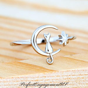 May include: A silver ring with a crescent moon design featuring a cat sitting on the moon and a star to the side.