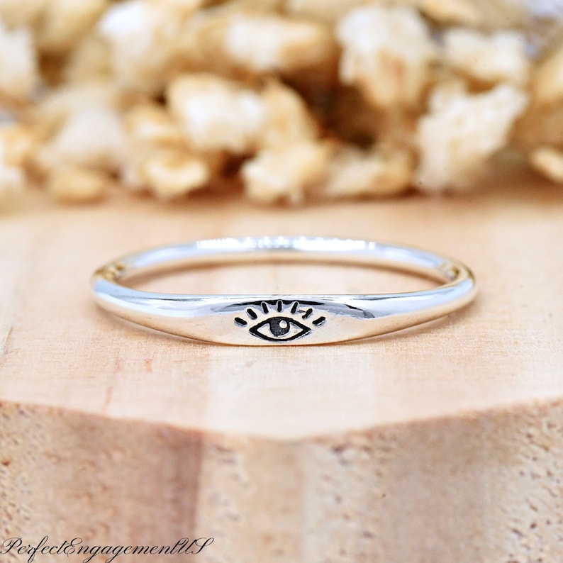 May include: A silver ring with a simple eye design. The ring is thin and delicate, and the eye is centered on the band.