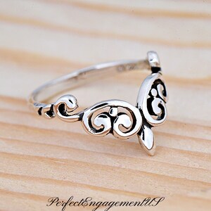 May include: A silver ring with a delicate, ornate design. The ring is made of a thin band with a decorative, openwork design that resembles a stylized flower or leaf.