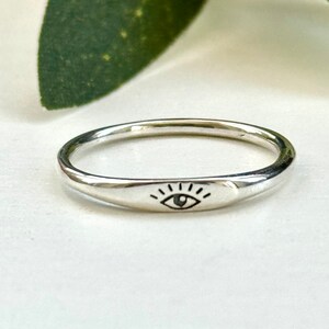 May include: A silver ring with a simple eye design engraved on the band.