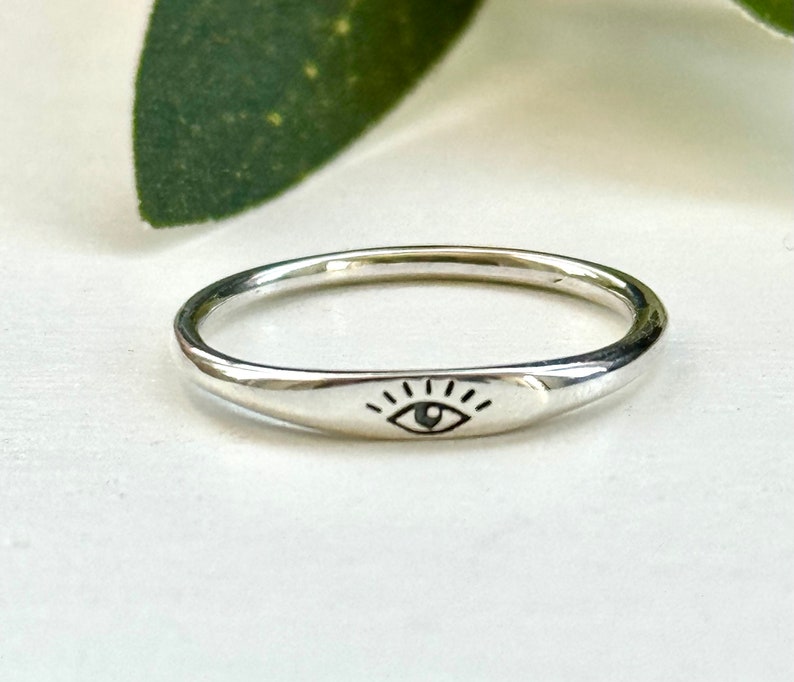 May include: A silver ring with a simple eye design engraved on the band.