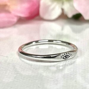 May include: A silver ring with a simple eye design. The ring is thin and delicate, and the eye is centered on the band.