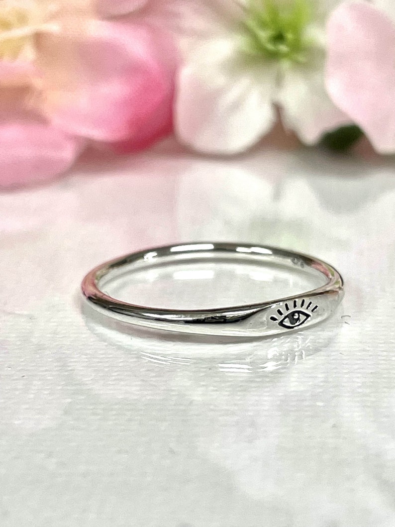 May include: A silver ring with a simple eye design. The ring is thin and delicate, and the eye is centered on the band.