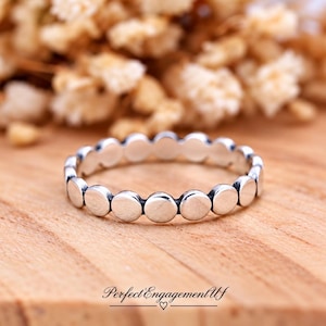 May include: A silver ring featuring a continuous band of small, circular, polished metal discs linked together. The ring has a bright, reflective finish and a uniform, repeating pattern of round elements encircling the entire band.
