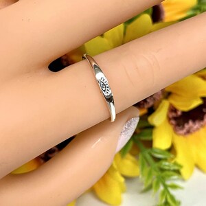 May include: A silver ring with an eye design. The ring is on a finger and the background is blurred.