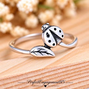 May include: A silver ring featuring a ladybug design with black spots and a leaf motif. The band is polished silver, and the ladybug is positioned on one side of the ring, while the leaf extends from the other side, creating a nature-inspired look.