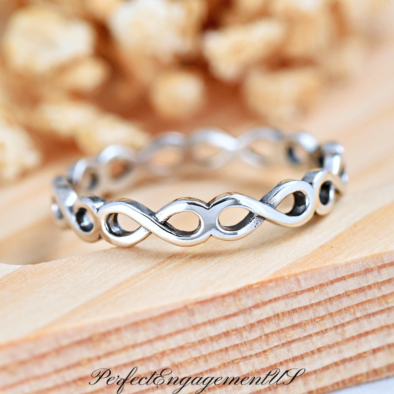 May include: A silver ring with a delicate, interwoven design. The ring is made of a smooth, polished metal and has a simple, elegant style.