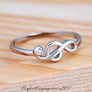 May include: A silver ring with an infinity symbol and a small clear stone. The ring is on a wooden surface.