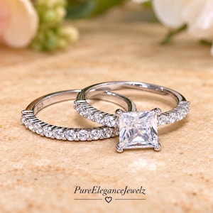 May include: A silver-toned engagement ring set featuring a princess-cut center stone and a matching band, both adorned with small round pavé-set stones. The inner band is stamped with 925, and the text PureEleganceJewelz is visible below.