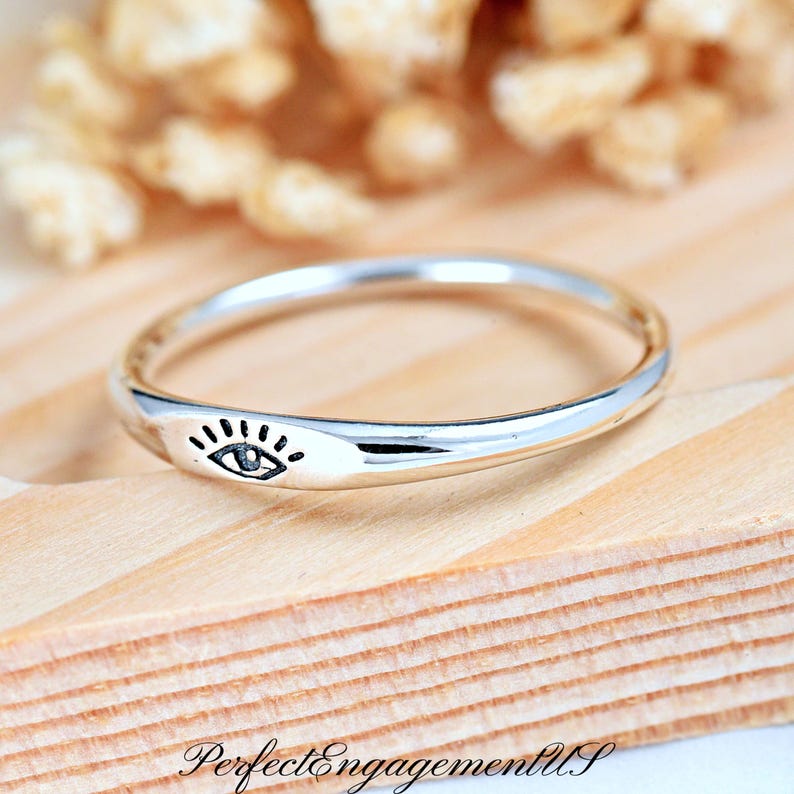 May include: A silver ring with a simple eye design. The ring is thin and delicate, and the eye is centered on the band.