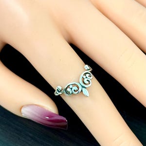 May include: A silver ring with a delicate, ornate design. The ring is shaped like a crown with a pointed tip.